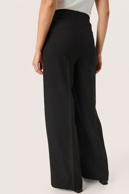 Rückansicht der Soaked Corinne Wide Long Pants - Black, elegante schwarze Hose mit weitem Bein und elastischem Bund für hohen Tragekomfort.