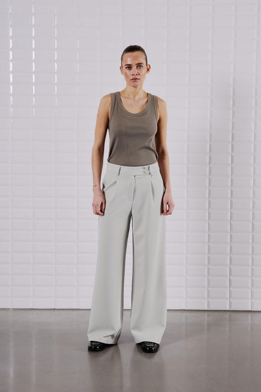 Model trägt das WithBlack Lulu Tank Top Light Stone Grey kombiniert mit einer weiten Stoffhose in Beige.