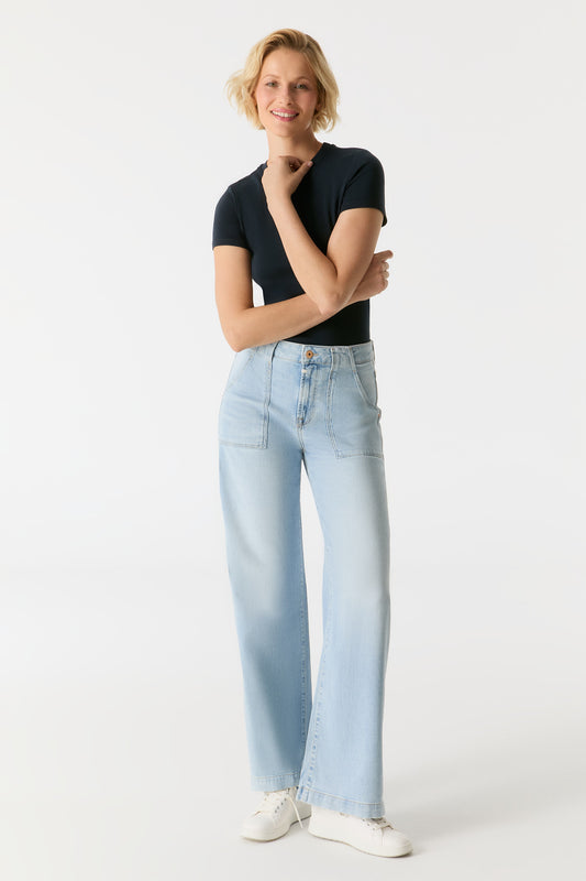 Model trägt die COJ Lulu Wide Leg Aqua Blue Jeans in voller Länge, kombiniert mit einem schwarzen Shirt und weißen Sneakern.