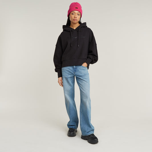 Model trägt die G-Star Judee Loose Jeans in Faded Brilliant Blue mit schwarzem Hoodie und pinker Mütze.