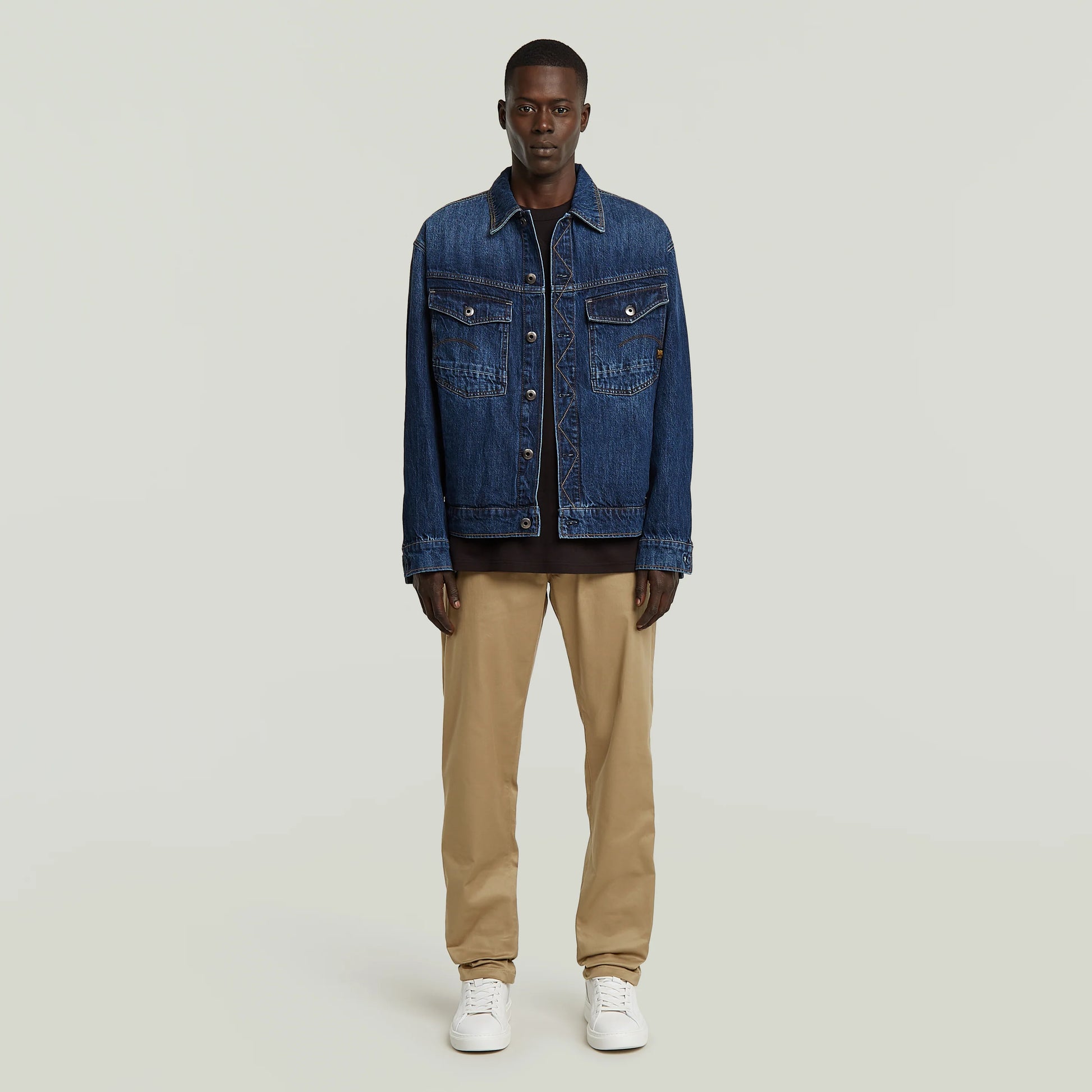 Modell trägt G-Star Morry Tapered Chino Safari mit dunkler Denimjacke und weißen Sneakers.
