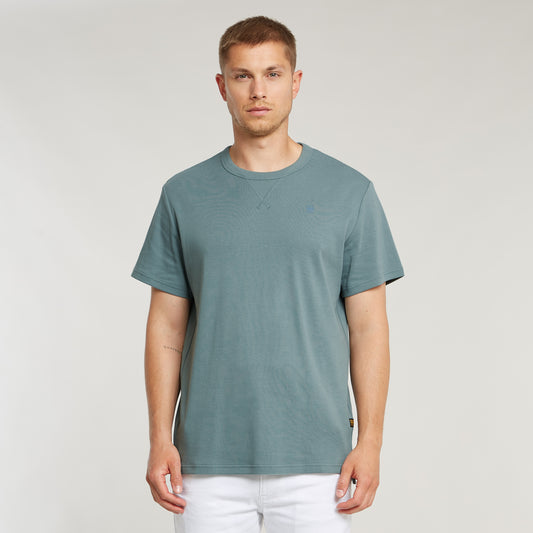 Model trägt das G-Star Nifous T-Shirt in Bolt Grey mit weißer Hose, zeigt die Passform und den Schnitt des Shirts.