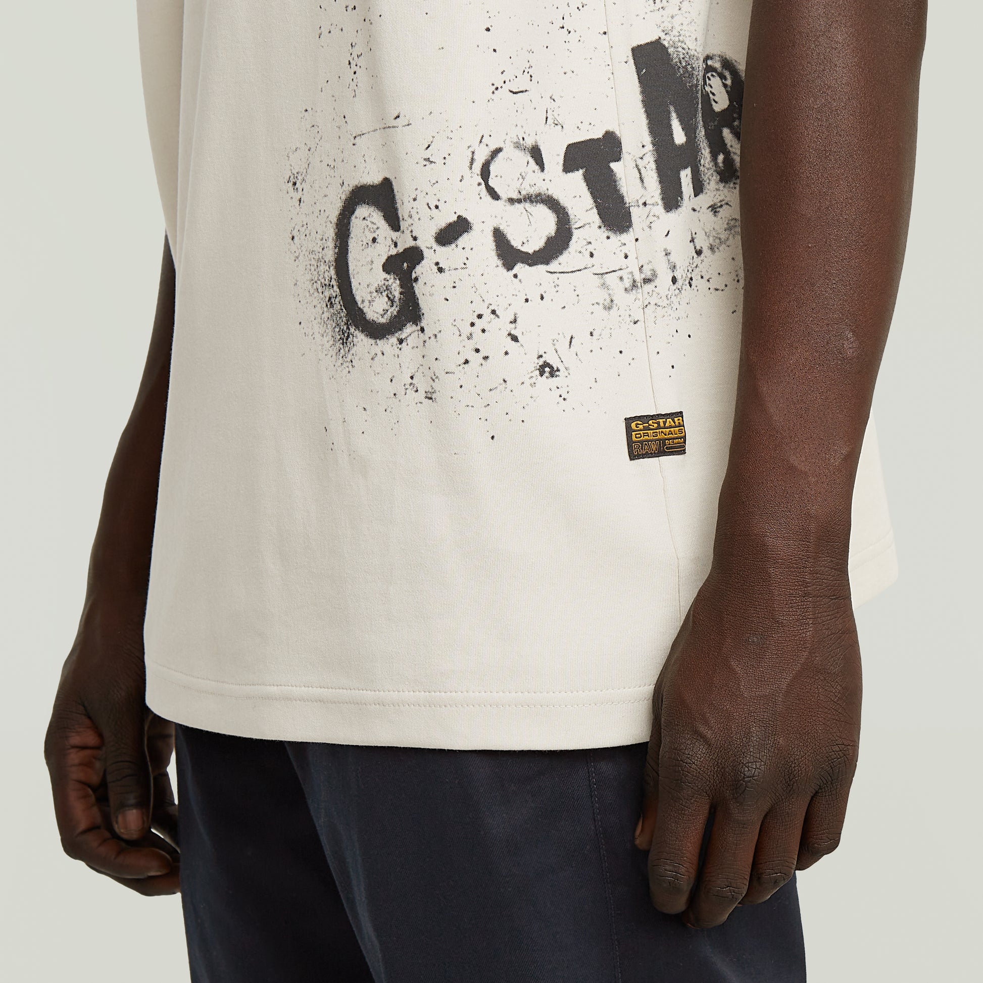 Detailansicht des G-Star Raw Sprayed T-Shirt - Whitebait mit schwarzem Spray-Logo-Print und Markenlabel.