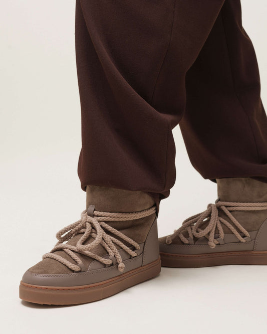Inuikii Classic Taupe Winterboots – am Fuß getragen, kombiniert mit brauner Hose, zeigt den lässigen Winterlook.