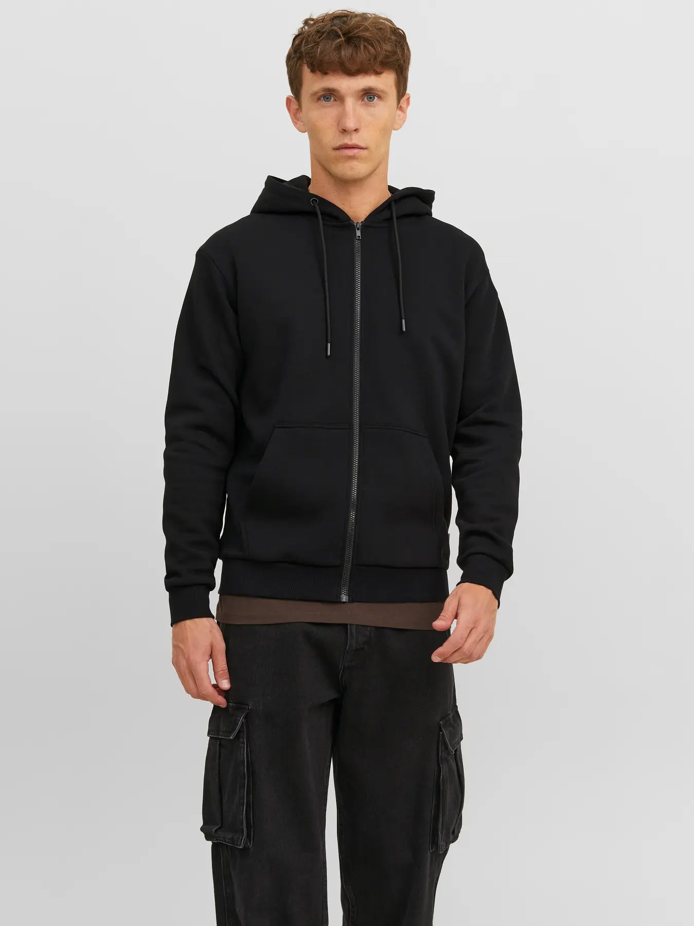 Model trägt den Jack&Jones Bradley Sweat Zip Hood Black, einen schwarzen Zip-Hoodie mit Kängurutaschen und Kapuze.