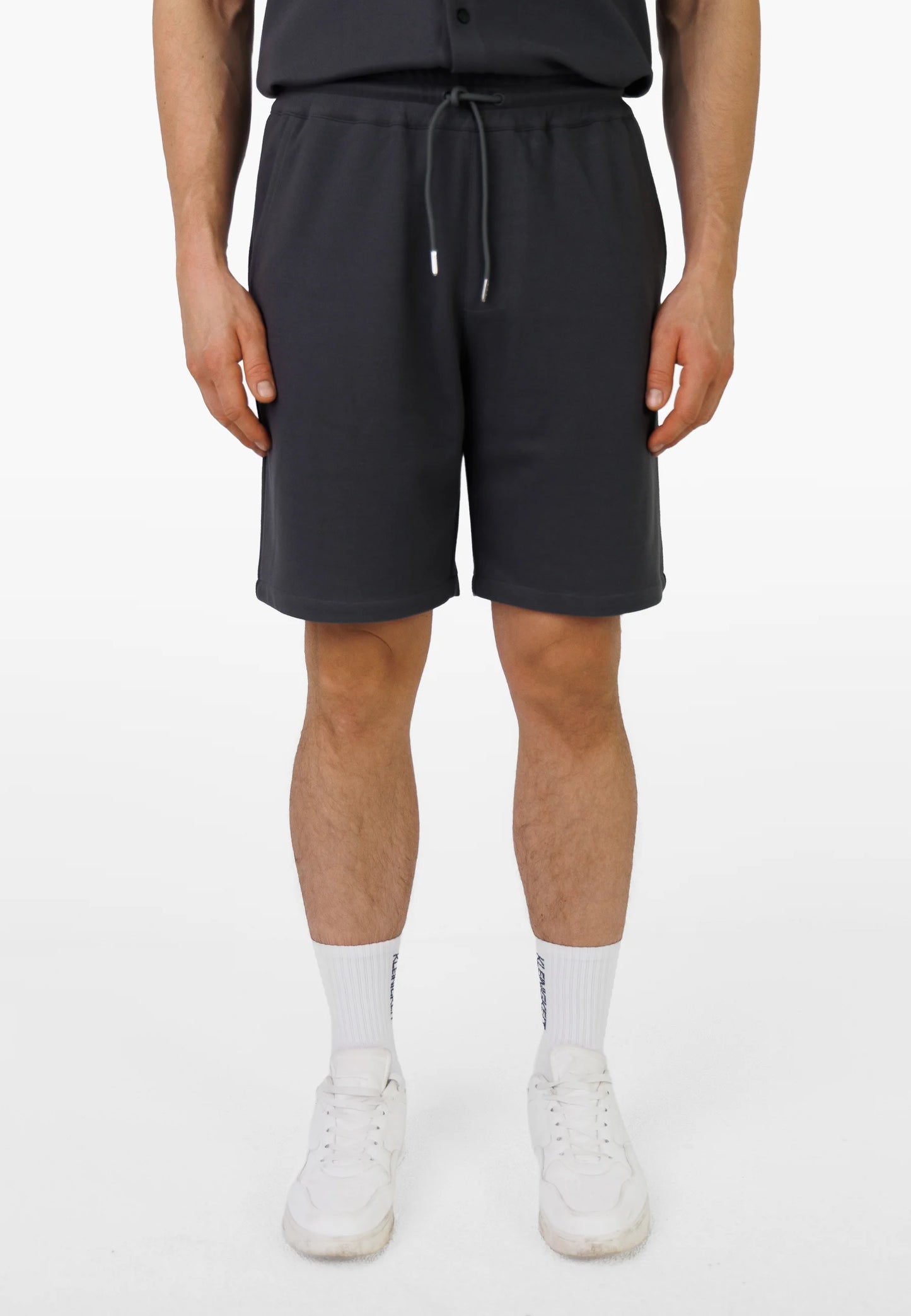 Modell trägt die Kleinigkeit Relaxel Schulz Shorts - Asphalt Grey im kompletten Sommer-Outfit mit passendem Shirt und Sneakern.
