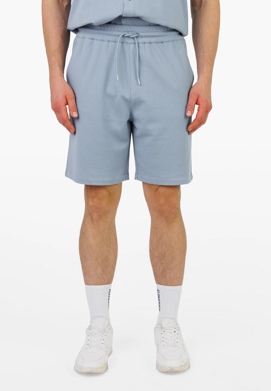 Modell trägt die Kleinigkeit Relaxel Schulz Shorts - Breeze Blue in der Vorderansicht mit elastischem Bund und modernem Schnitt.