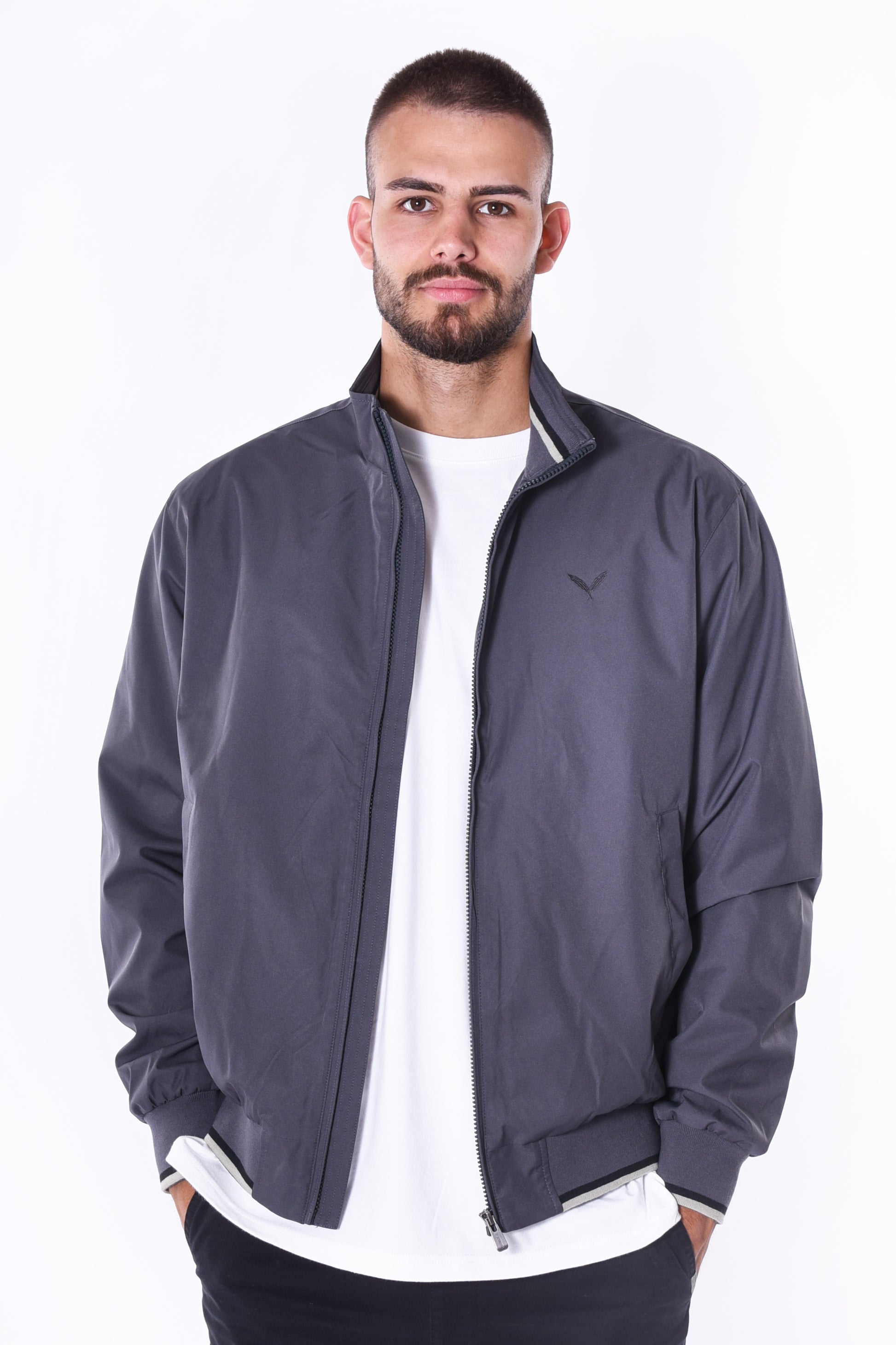 Modell trägt die Kleinigkeit Signature Jacket Ashphalt Grey mit Stehkragen, gerippten Abschlüssen und dezentem Ton-in-Ton Feather-Logo auf der Brust.