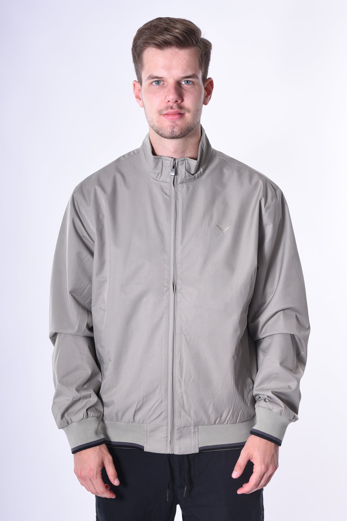 Modell trägt die Kleinigkeit Signature Jacket Olive mit Stehkragen, gerippten Abschlüssen und dezentem Ton-in-Ton Feather-Logo auf der Brust.