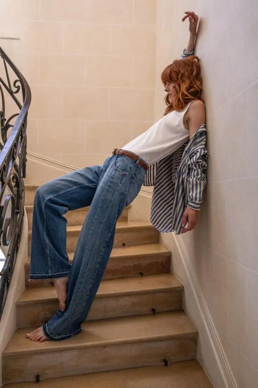 Model trägt die Le Temps Des Cerises Lauryn Mid Waist Wide Leg Jeans in Aix Blue N4 in einer lässigen Lifestyle-Szene auf einer Treppe.
