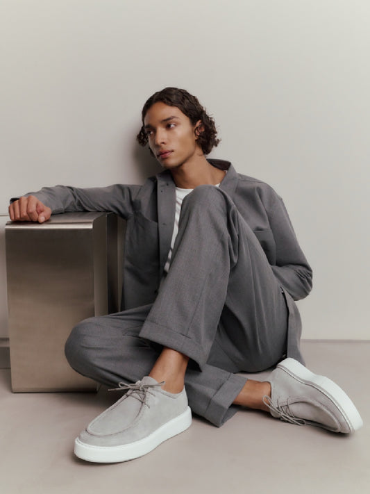 Model mit grauem Outfit und Nubbik Vince Ryan Light Grey Suede Schuhen, lässig angelehnt