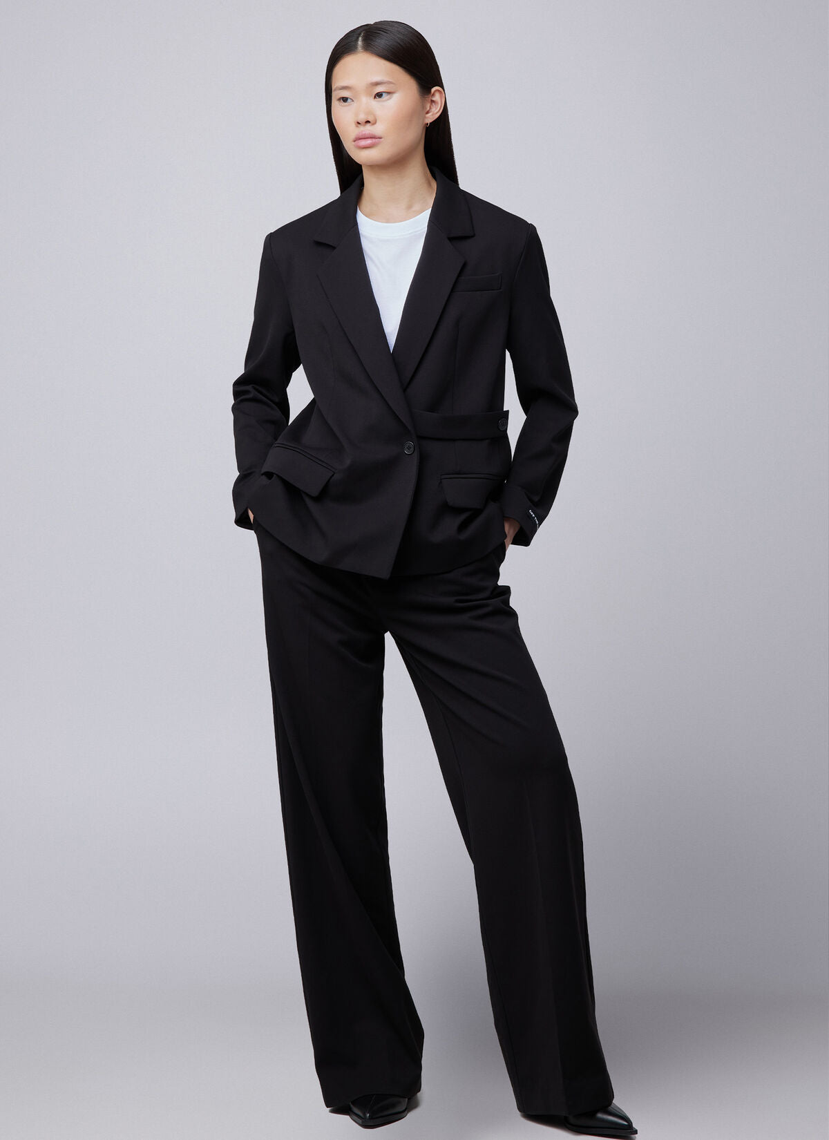 Off the Pitch Pleated Gaia Pants Black – am Modell getragen, kombiniert mit schwarzem Blazer und weißem Shirt für einen modernen Business-Look.