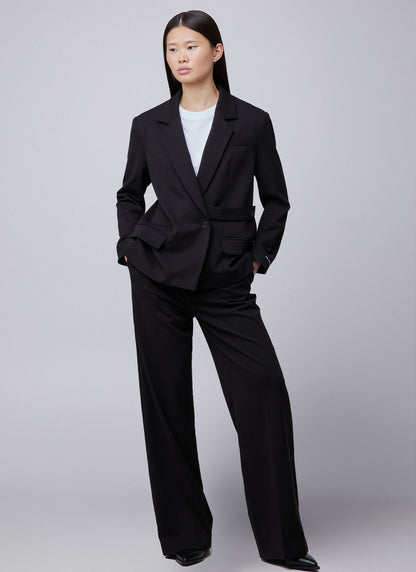 Off the Pitch Pleated Gaia Pants Black – am Modell getragen, kombiniert mit schwarzem Blazer und weißem Shirt für einen modernen Business-Look.