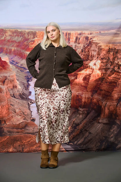 Model trägt den Only Carmakoma Domina Satin Calf Skirt – Texana Dots in stilvoller Kombination mit Strick und Boots. Perfekt für elegante Casual-Looks.