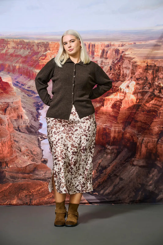 Model trägt den Only Carmakoma Domina Satin Calf Skirt – Texana Dots in stilvoller Kombination mit Strick und Boots. Perfekt für elegante Casual-Looks.