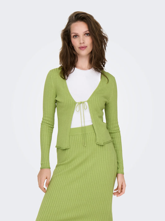 Model trägt den Only Mila Cardigan Leaf Green, einen grünen Rippstrick-Cardigan mit Bindeband vorne, kombiniert mit einem weißen Oberteil und einem passenden grünen Rock.