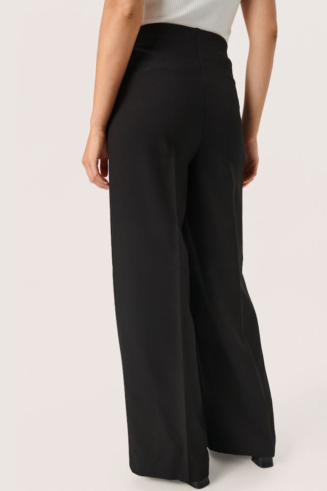 Rückenansicht der Soaked Corinne Wide Long Pants Black – weite, fließende Hosenbeine und hoher Bund für eine elegante Silhouette.