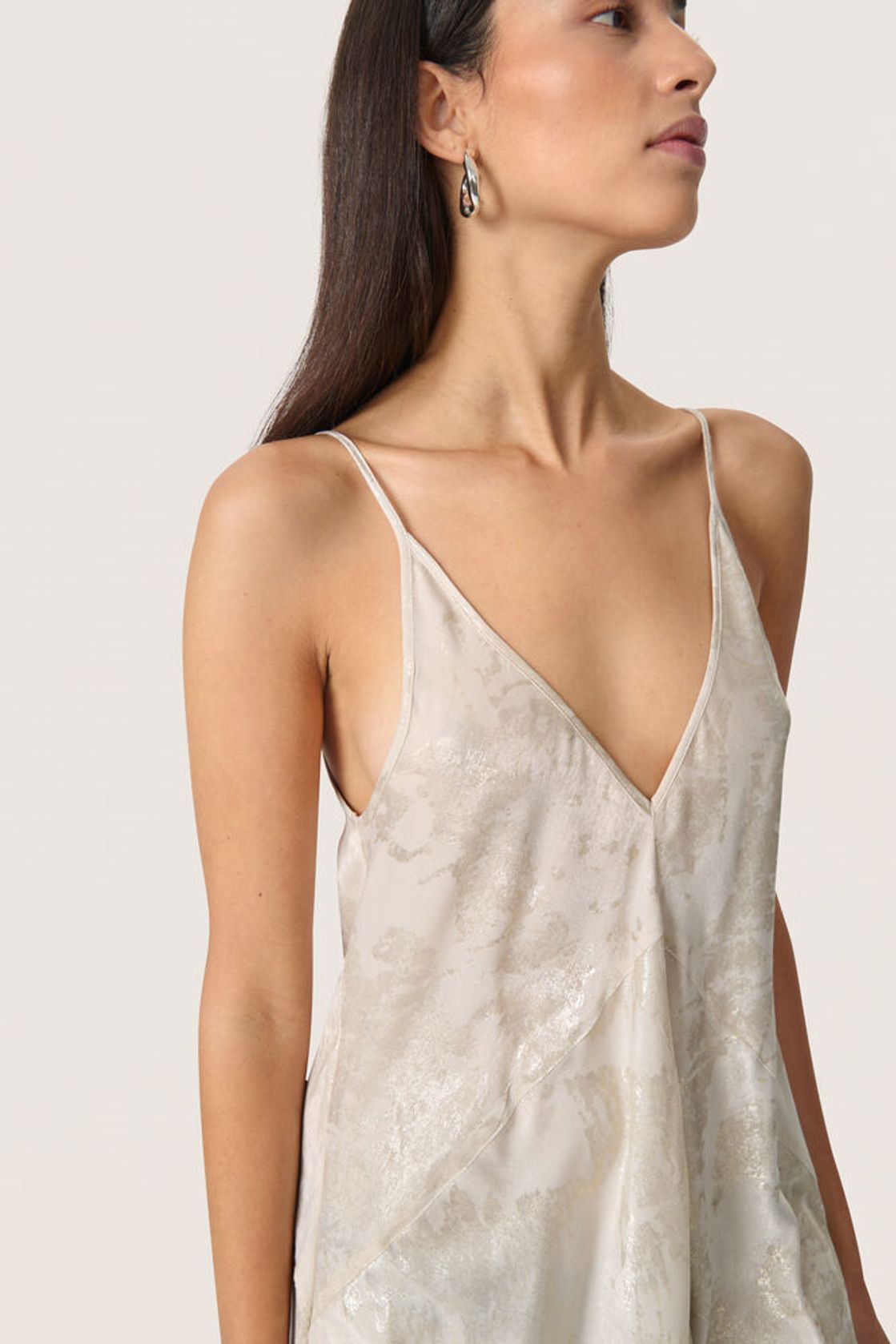 Detailansicht des tiefen V-Ausschnitts vorne beim Soaked Kitty Strap Dress - Ancient Scroll Metallic Print aus glänzendem Stoff.