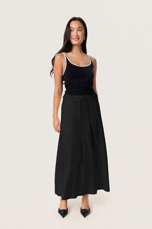Modell trägt den Soaked Malika Midi Skirt - Black von vorne, eleganter schwarzer Midirock mit hohem Bund und Gürtel