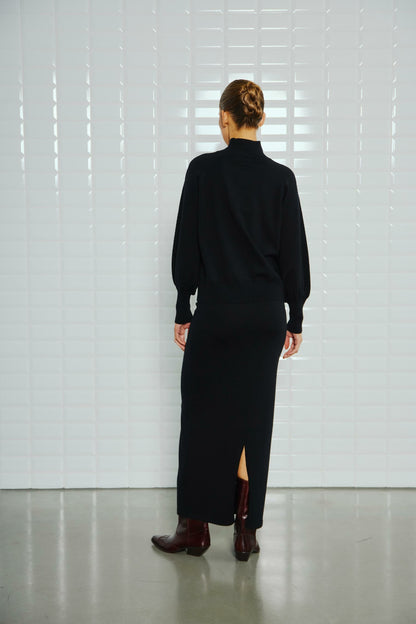 With Black Destiny High Neck Pullover Black – Rückansicht des schwarzen Pullovers mit hohem Kragen, kombiniert mit einem langen Rock und braunen Stiefeletten.