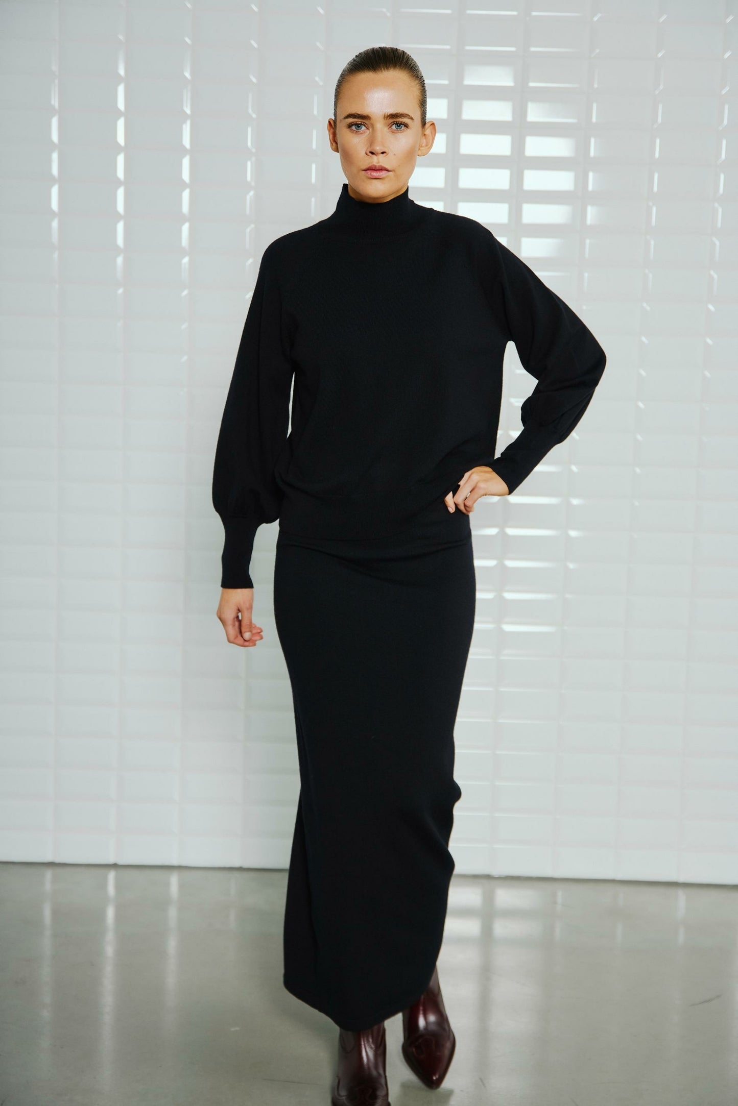 With Black Destiny High Neck Pullover Black – Vorderansicht des schwarzen Pullovers mit hohem Kragen und langen Ärmeln, elegant kombiniert mit einem schwarzen Maxi-Rock.