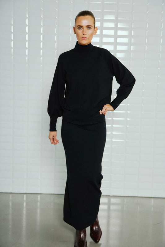 With Black Destiny High Neck Pullover Black – Vorderansicht des schwarzen Pullovers mit hohem Kragen und langen Ärmeln, elegant kombiniert mit einem schwarzen Maxi-Rock.