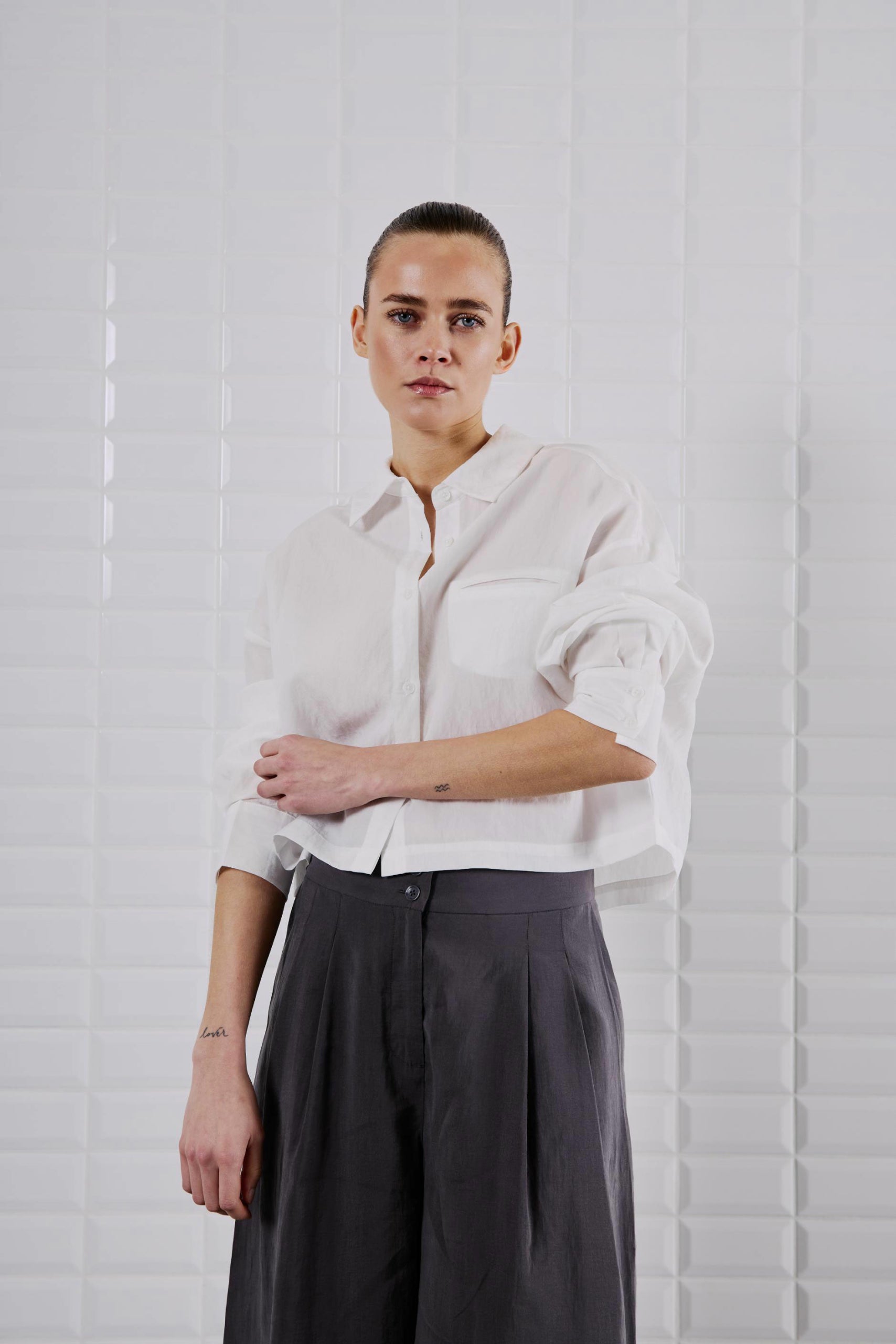 Frontansicht des WithBlack Quinie Cropped Shirt White, locker geschnitten mit Brusttasche, kombiniert mit weiter schwarzer Hose.